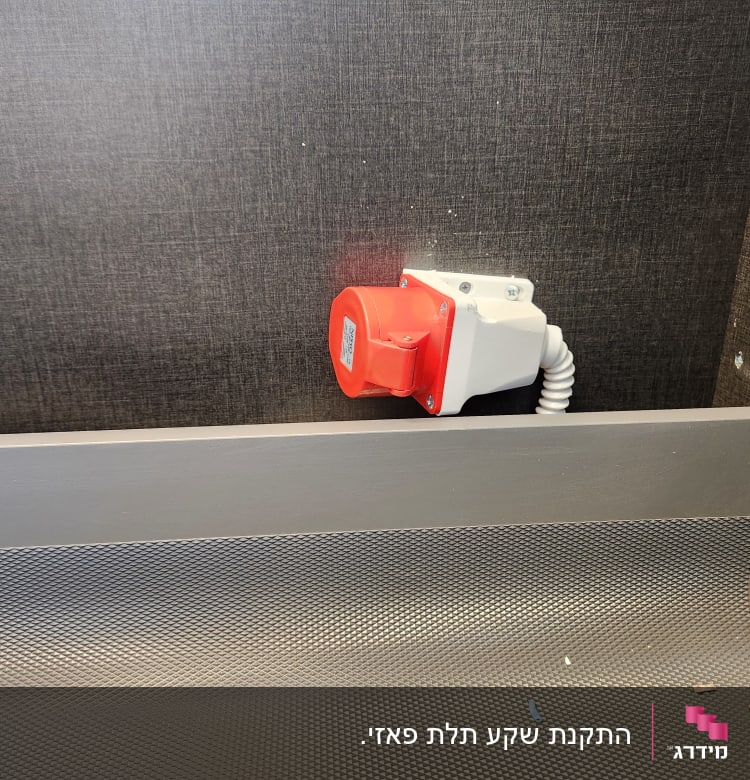 שקע חשמלי תעשייתי עם כיסוי אדום על קיר אפור